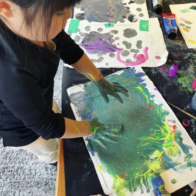 手に緑色の絵の具を塗って紙に手で色を付けている女の子